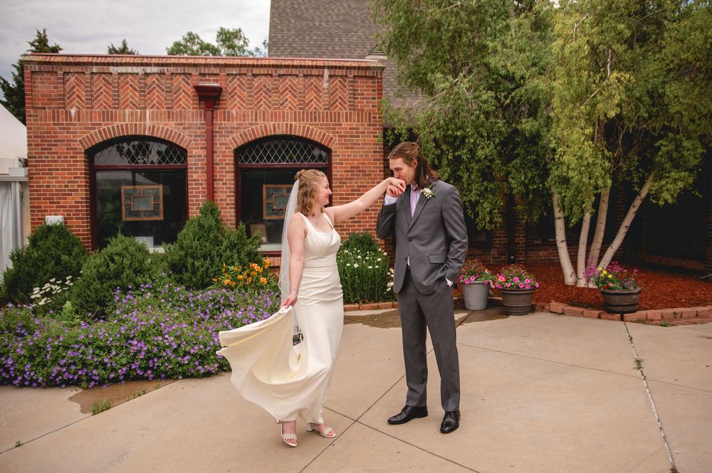 Couple standing on a tree-lined brick patio on their wedding day outside a historic brick building.