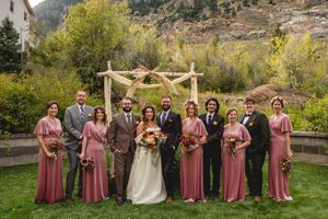 Wedding party in mauve bridesmaid dresses poses on grass with mountain backdrop in Colorado.