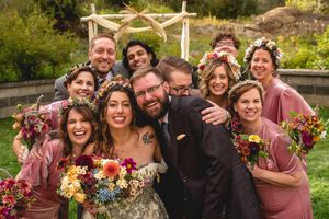 Wedding party poses together outdoors with colorful bouquets and mauve bridesmaid dresses.