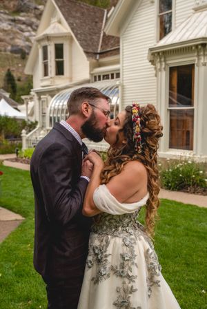 Romantic kiss in front of vintage white Victorian house with decorative trim.