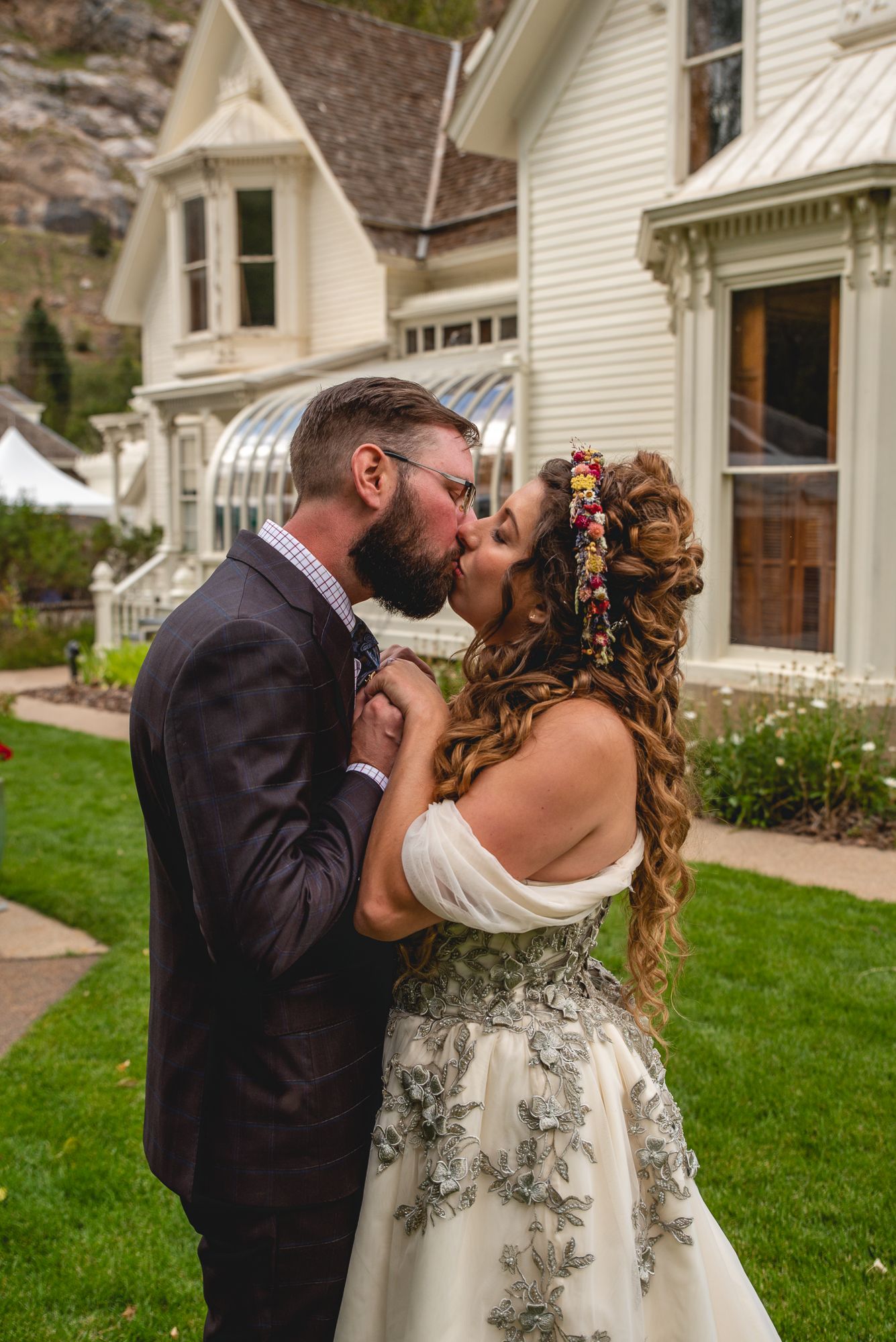 Romantic kiss in front of vintage white Victorian house with decorative trim.