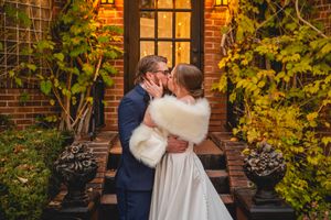 Wedding couple embraces on brick steps surrounded by autumn foliage.