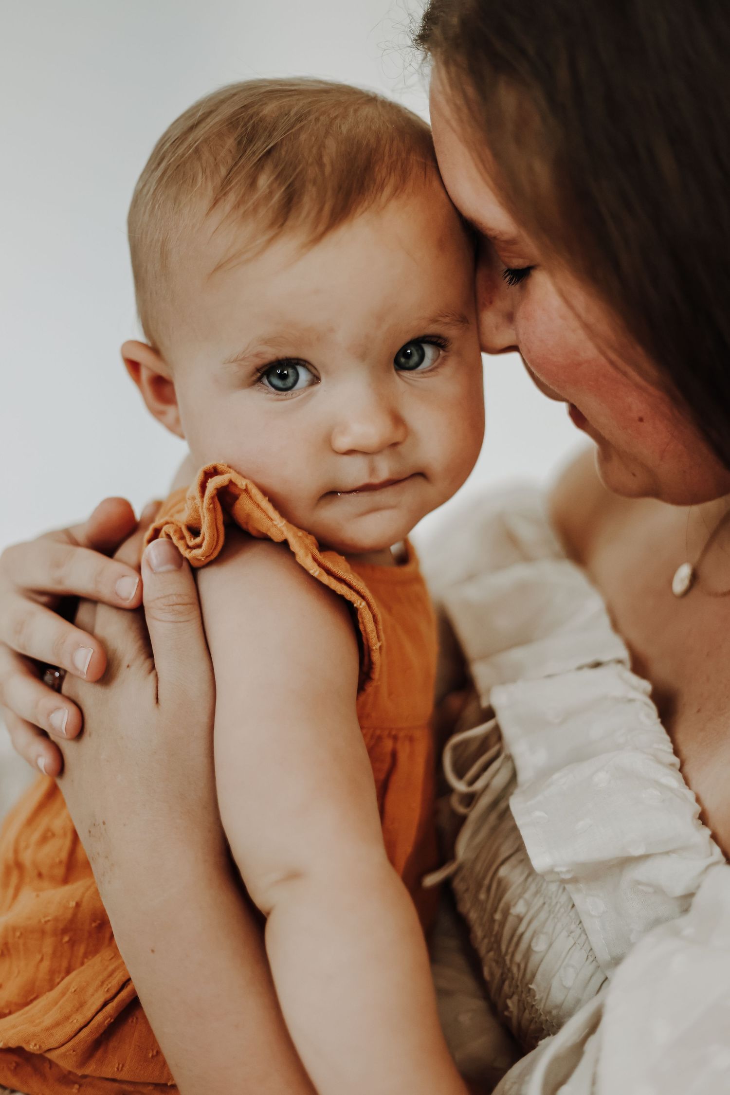 Tender moment between parent and baby in orange and white clothing. Family photography