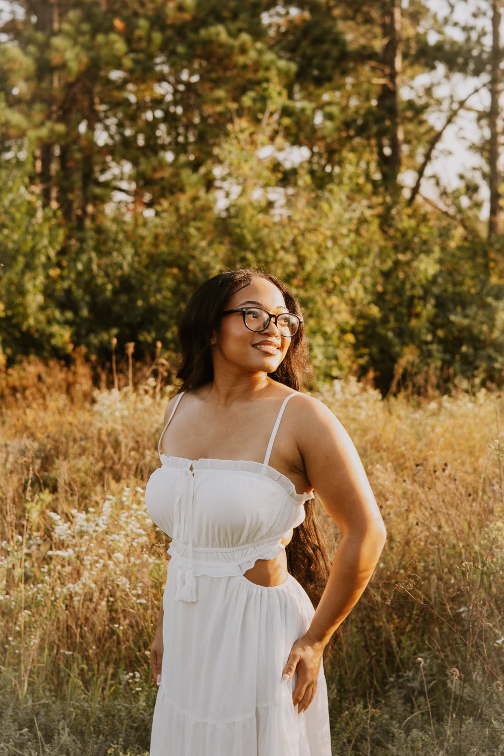 Person in white dress smiling in golden sunlit field during sunset.