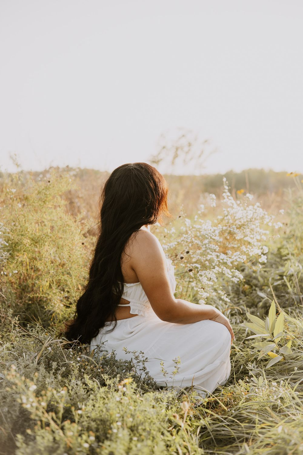Person in white dress sitting peacefully among wildflowers at sunset.