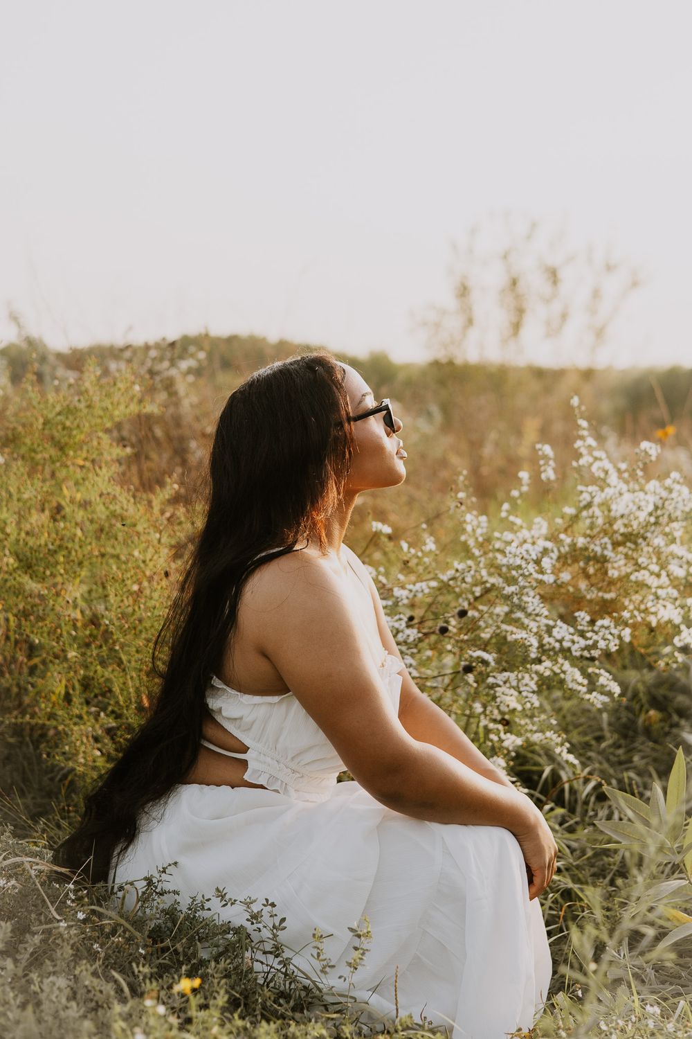Woman in flowing white dress poses gracefully in sunlit meadow.