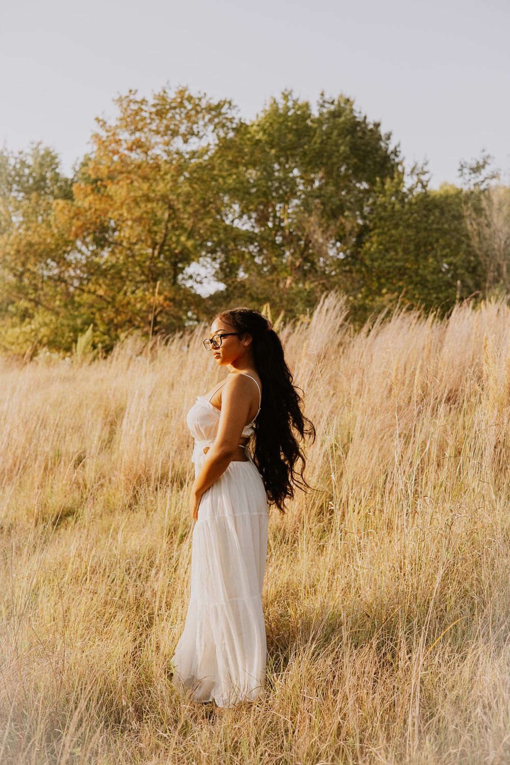 Figure in white dress walking through tall golden grass at sunset.