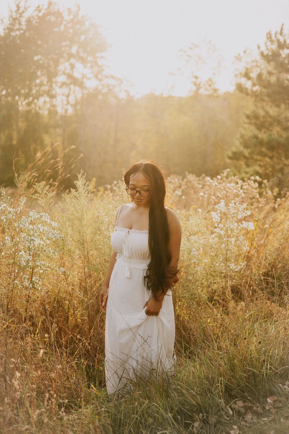 A white dress stands out against golden wildflowers and grass during sunset in a dreamy outdoor photoshoot.
