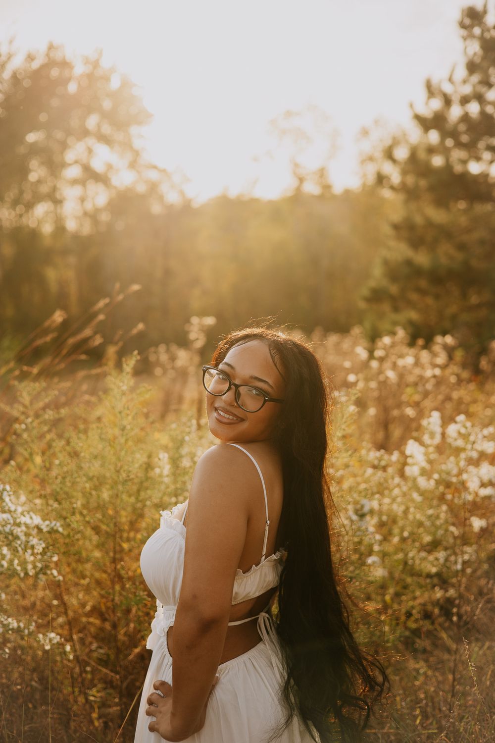 Joyful portrait in a sunlit meadow with white dress and glasses against warm evening light.