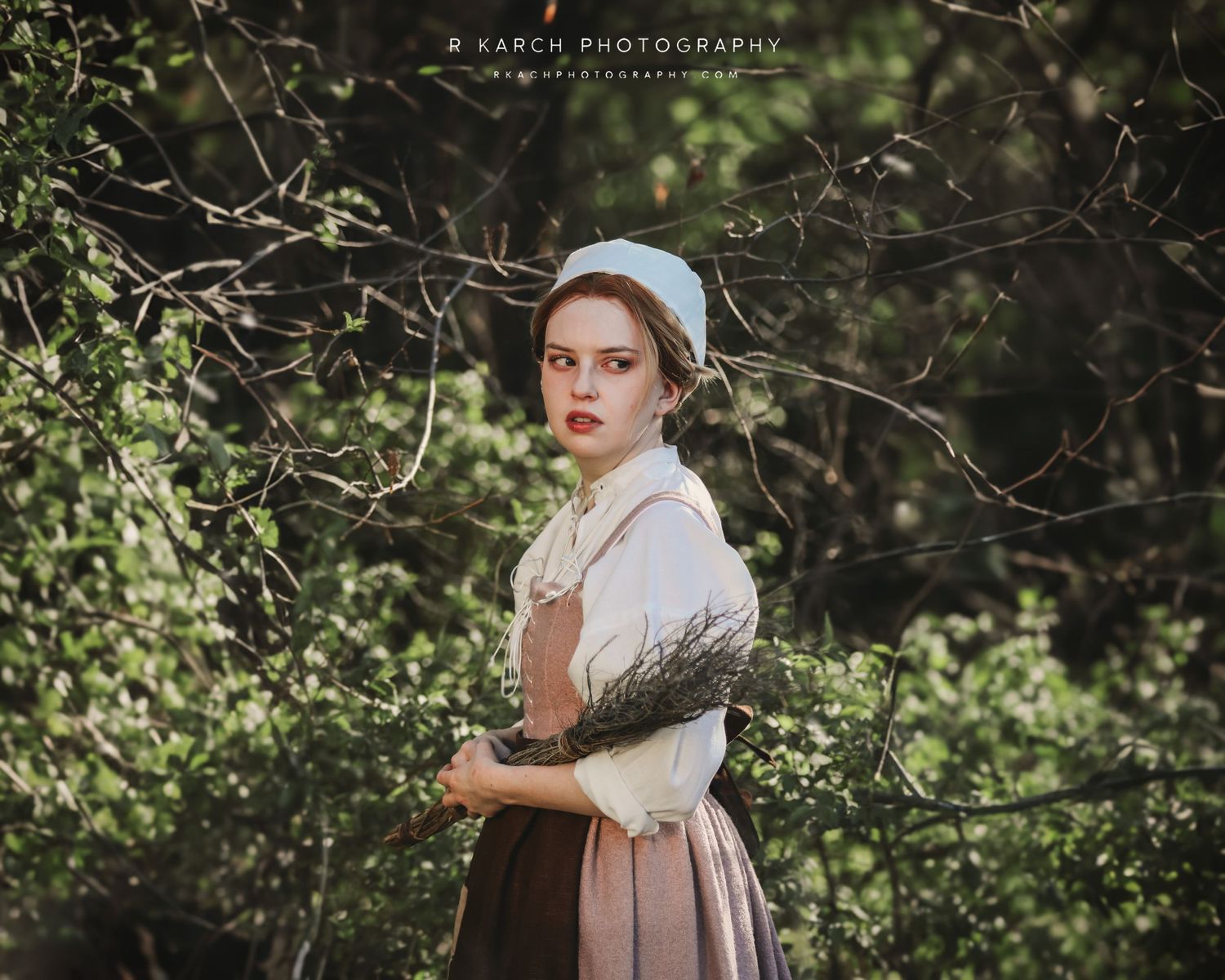 Pastoral portrait in vintage clothing with period dress and bonnet against blurred foliage background.