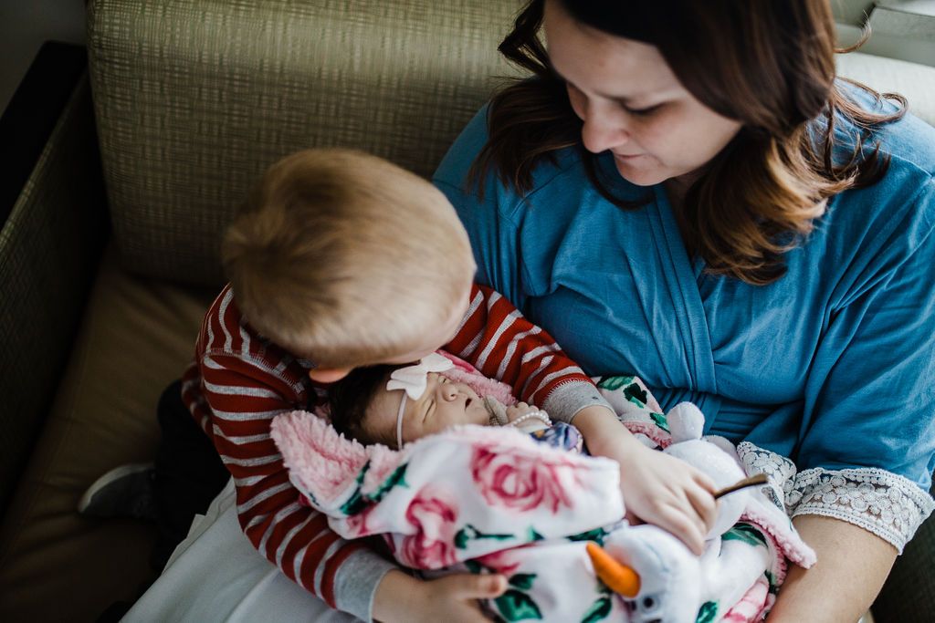 Parent and child bonding with newborn baby wrapped in floral blanket.