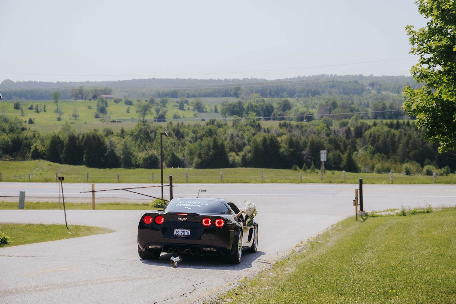 Black sports car driving on a rural road with rolling hills in background.