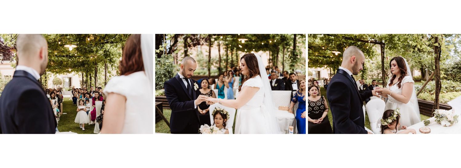 Outdoor wedding ceremony with couple exchanging rings surrounded by guests among lush green trees.