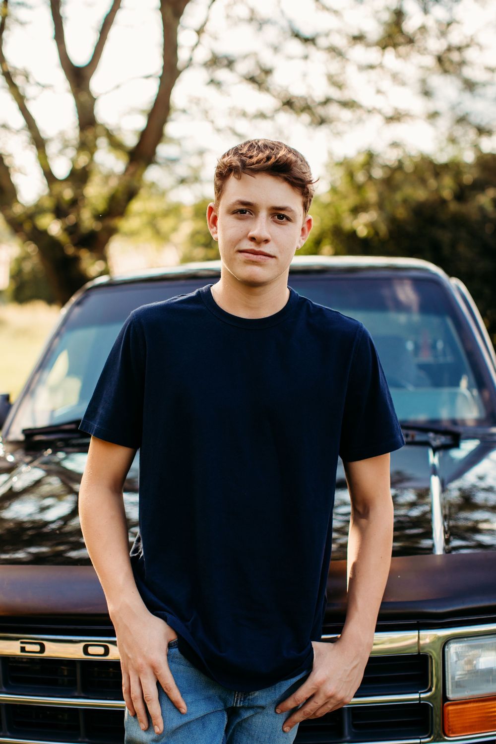 Person in navy t-shirt poses against vintage car during golden hour.