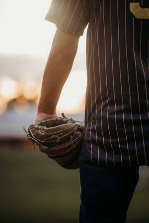 Baseball player in pinstripe jersey holding a worn leather glove at sunset on the field.