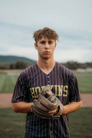 Young baseball player in Hopkins pinstripe jersey holding a Wilson glove on a field.