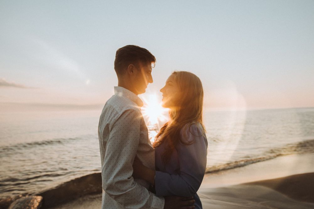 Silhouetted couple embracing on beach at sunset as golden light shines between them.