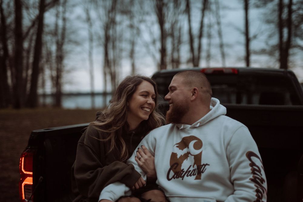 A couple laughing together while sitting in the back of a pickup truck near a lake.