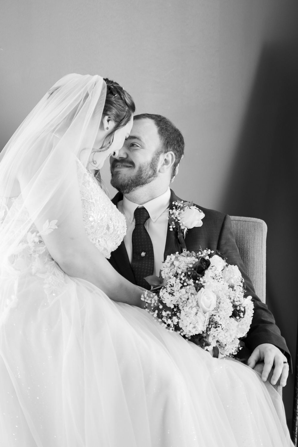 Black and white romantic portrait of bride and groom sharing an intimate moment with wedding bouquet.