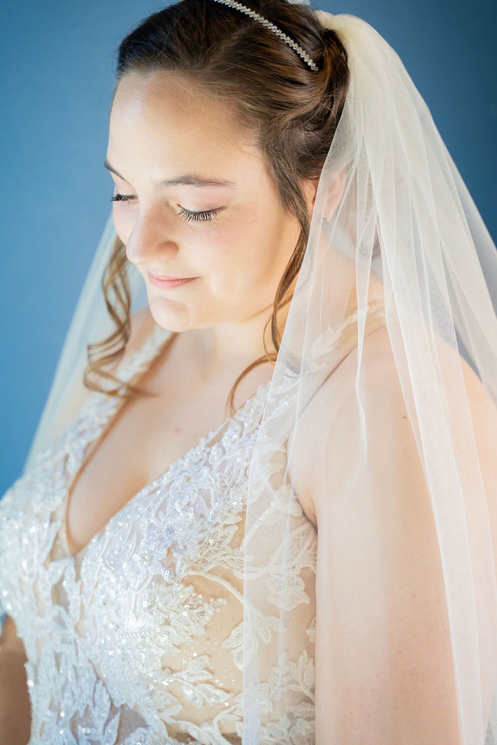 Close-up portrait of bride in lace gown and veil with eyes closed, serene expression.