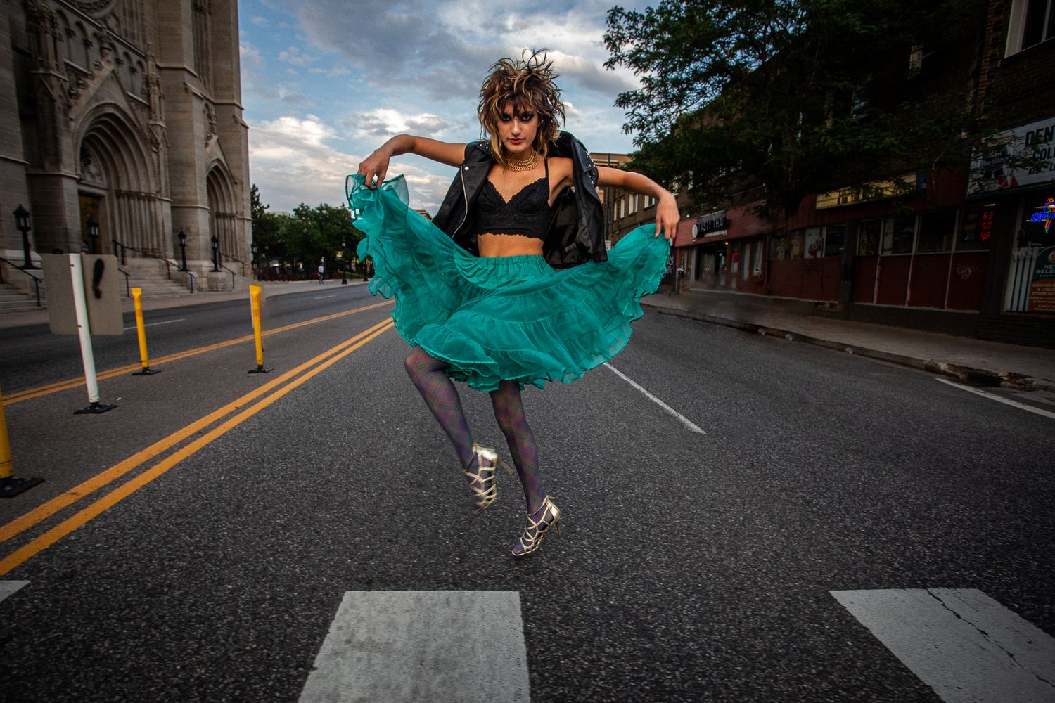 Dance-inspired fashion photo with model jumping in teal skirt on urban street.