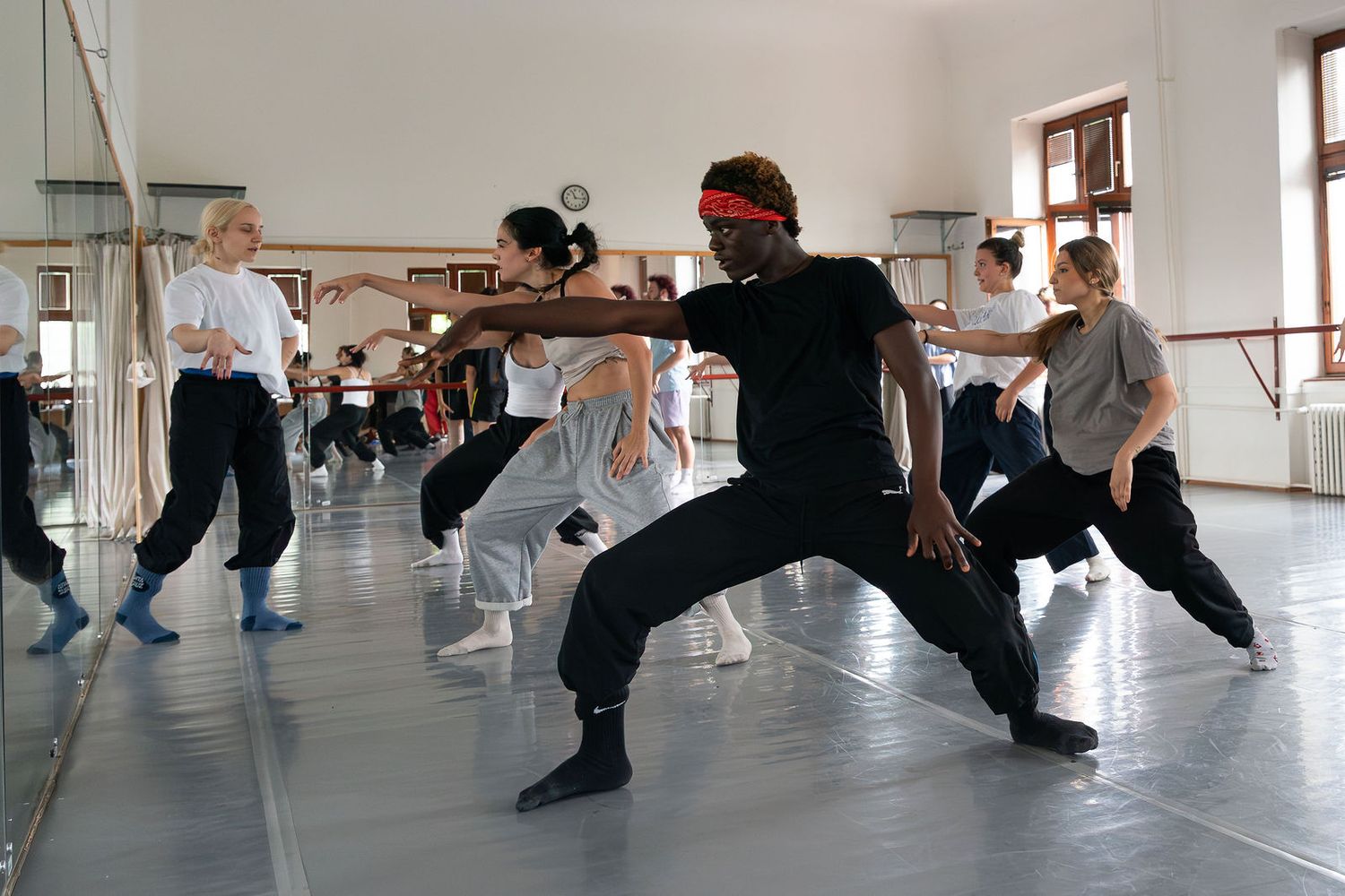 Diverse group of dancers rehearsing dynamic contemporary dance moves in a bright studio with ballet barres.