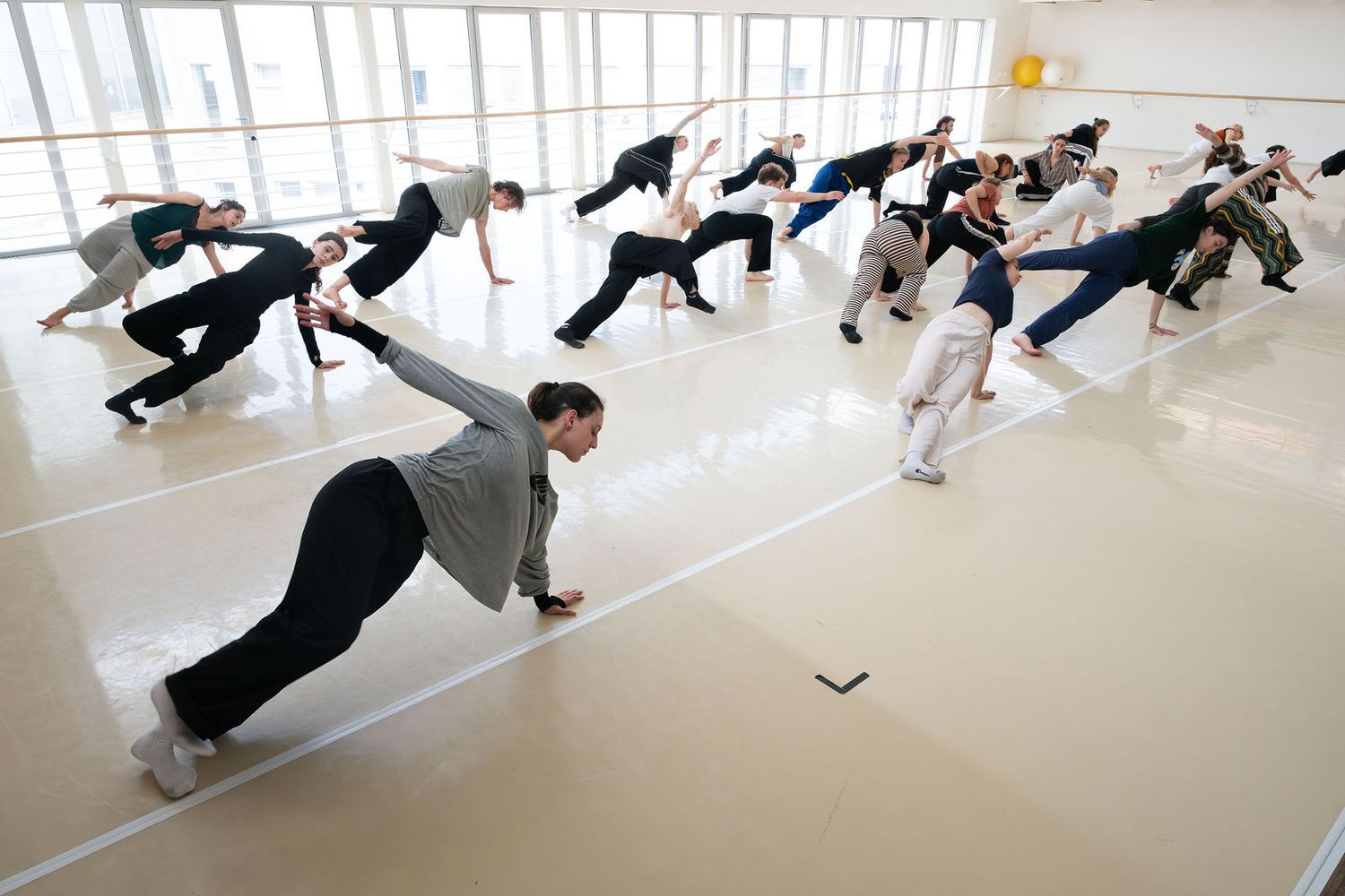Group of dancers practicing contemporary dance moves in a bright studio with mirrored walls and wooden floors.
