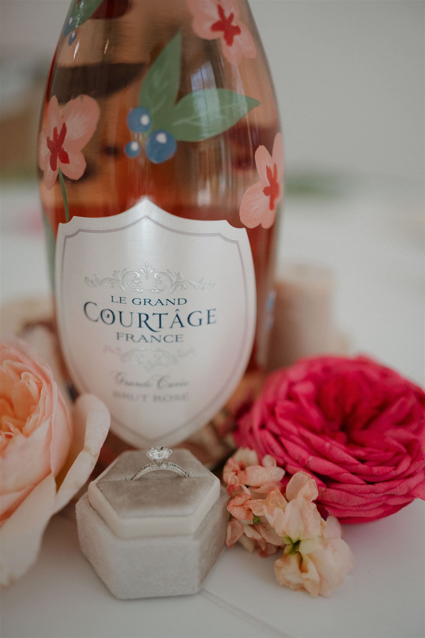 A bottle of Le Grand Courtage champagne decorated with floral patterns beside pink roses.