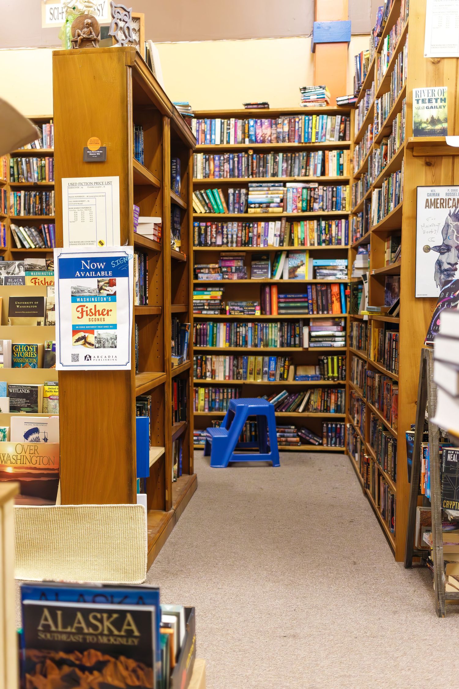Long rows of bookshelves in a bookstore with carpeted floors and wooden shelving units.