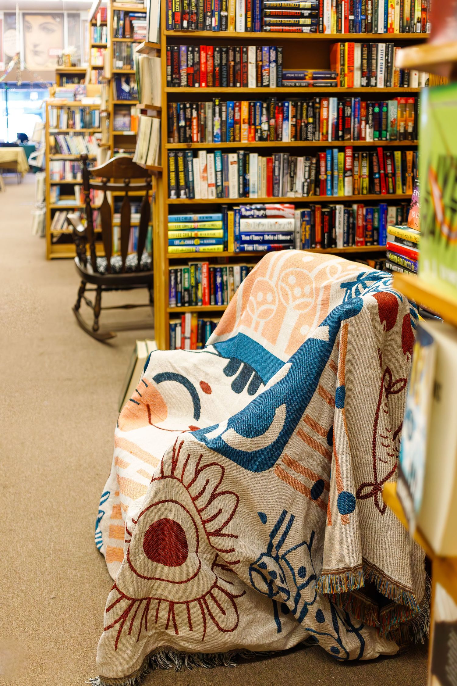 A cozy bookstore corner with wooden bookshelves and a decorative patterned blanket draped over a chair.