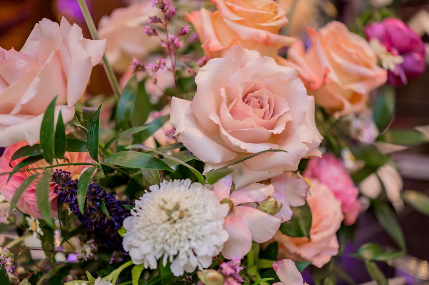 A floral bouquet features peach-colored roses, white dahlias, and pink wildflowers with green foliage arranged together.