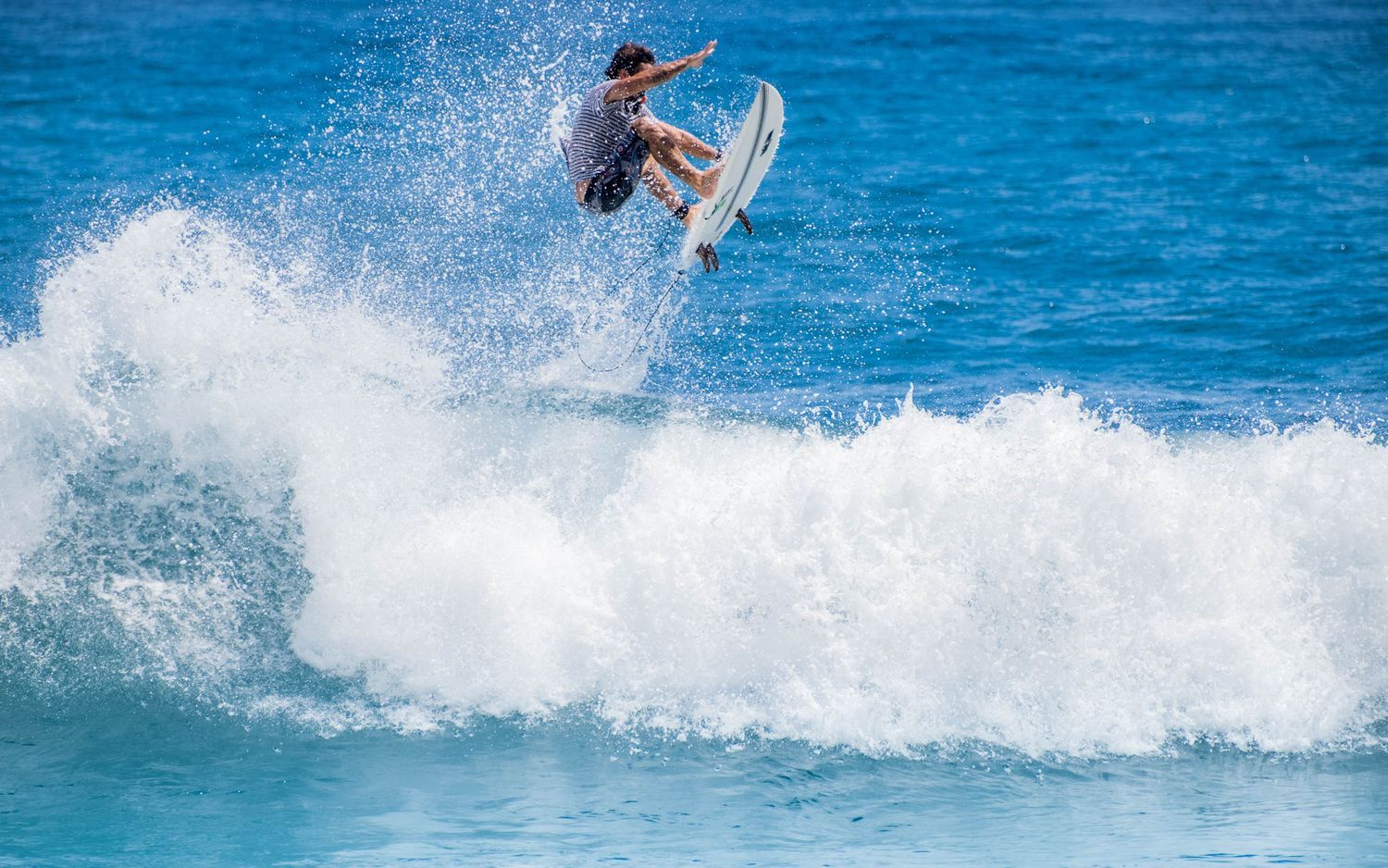 A surfer launches high into the air performing an aerial maneuver above a breaking wave.