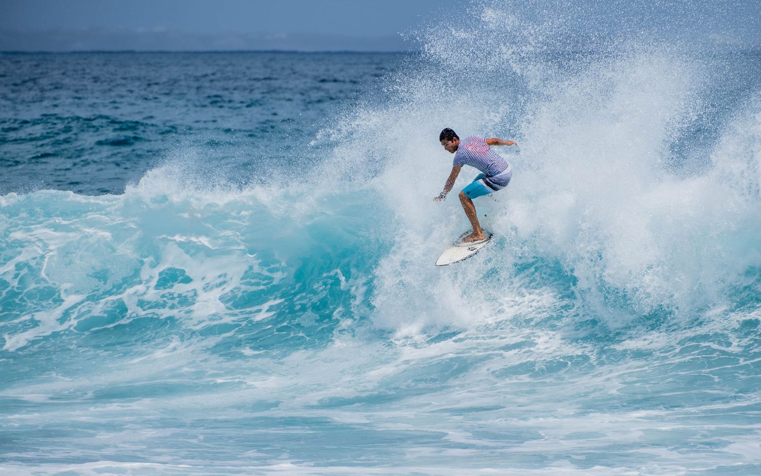 A surfer rides the face of a turquoise wave while performing a dynamic turn in tropical waters.