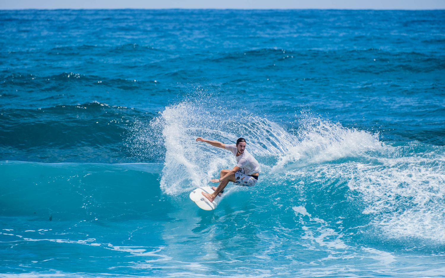 Surfer executing an aerial trick with spray flying off the turquoise wave.