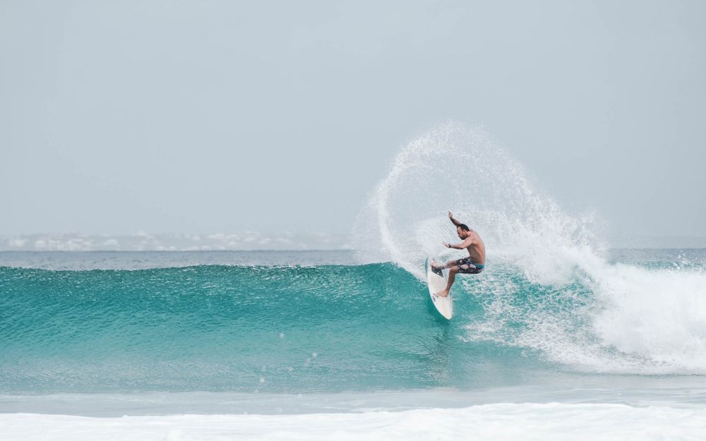 Surfer executes an impressive aerial maneuver above a breaking turquoise wave.
