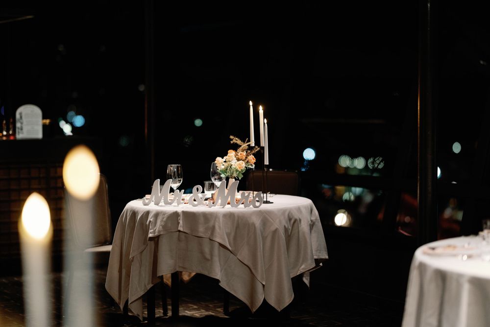 Romantic candlelit wedding sweetheart table with floral centerpiece and tall taper candles in a dark reception hall.
