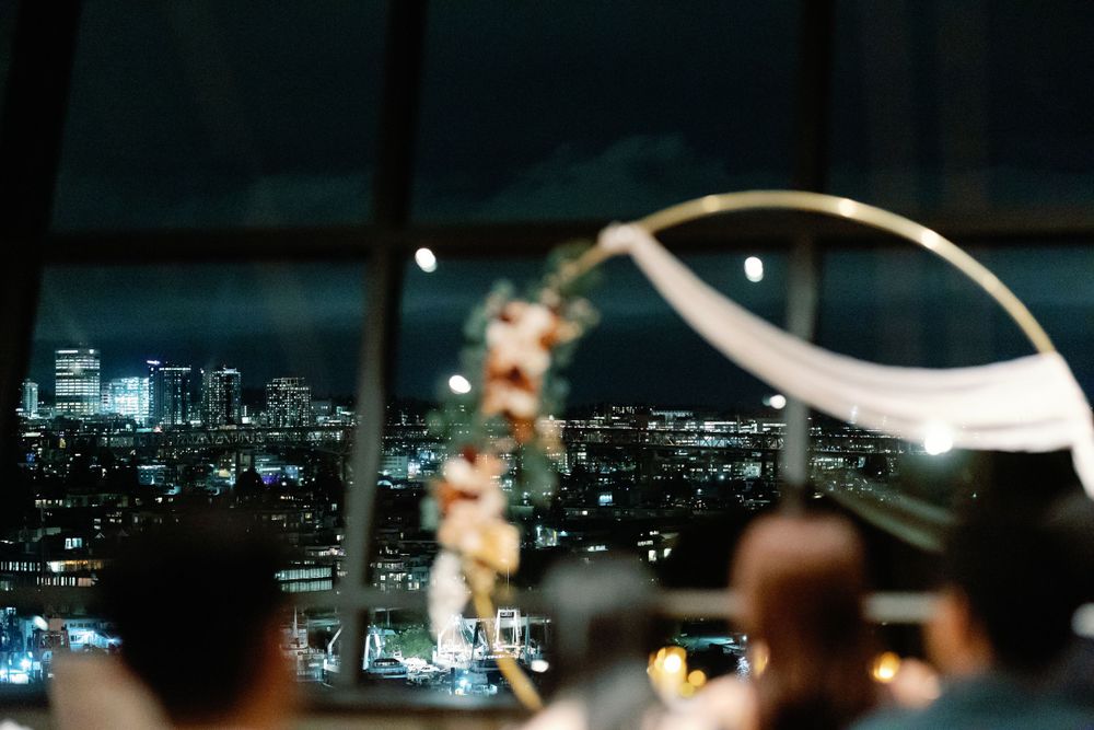Elegant wedding reception venue with city skyline views at night featuring floral arch centerpiece.