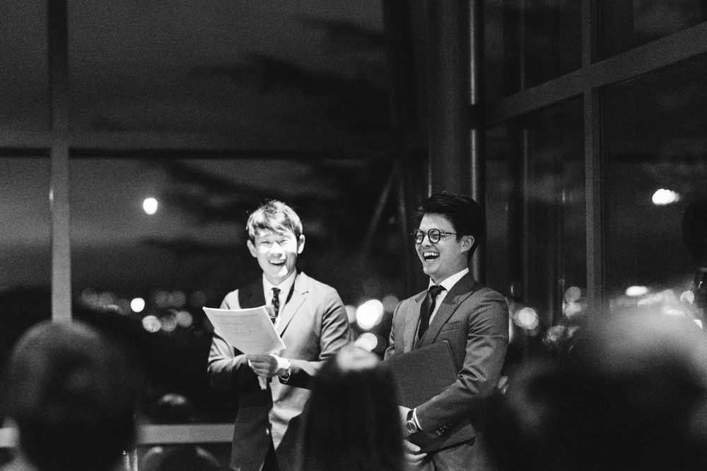 Two men in suits giving speeches at a nighttime wedding reception in black and white photo.