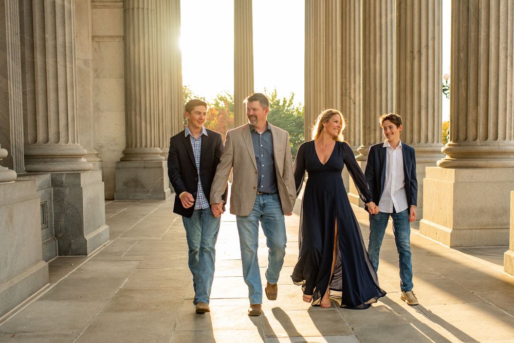 People walking through classical stone colonnade with dramatic lighting.