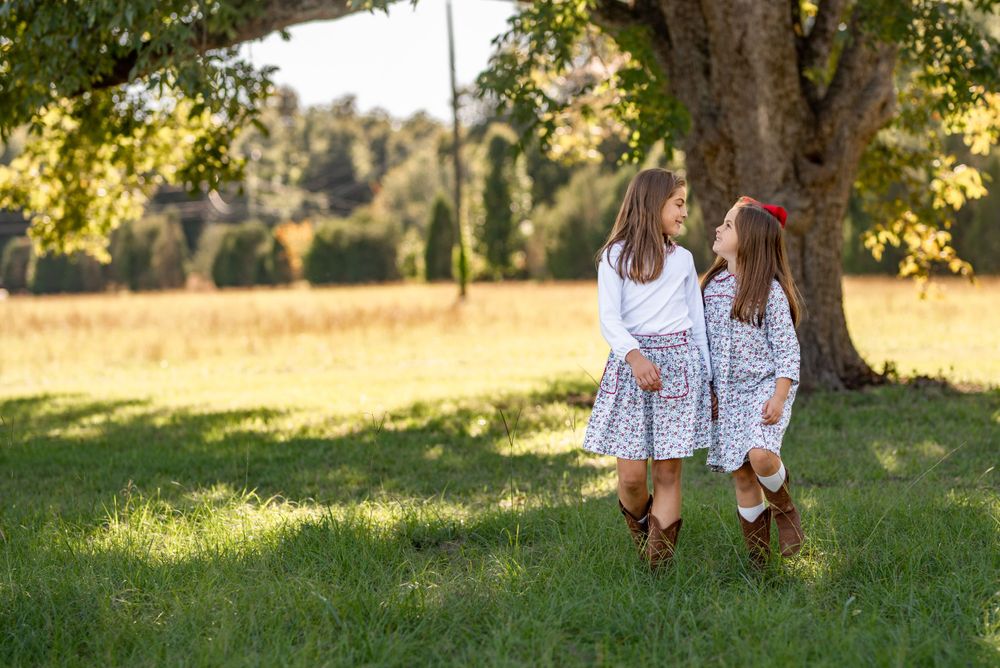 Children playing and running through sunlit grass near trees.
