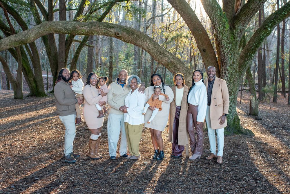 Extended family poses together under trees in coordinated neutral outfits.