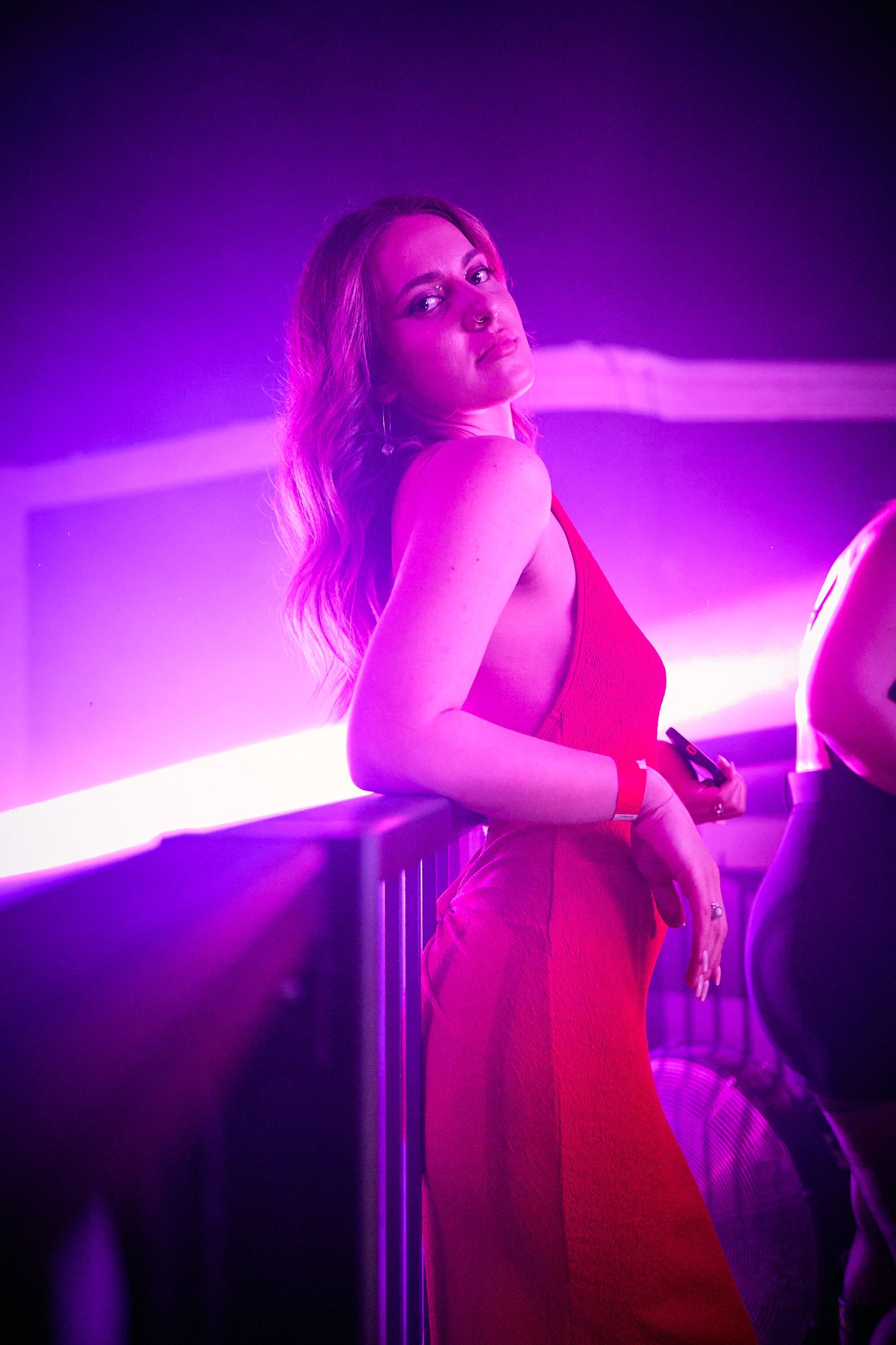 Atmospheric nightclub scene with figure in red dress illuminated by vibrant purple lighting.