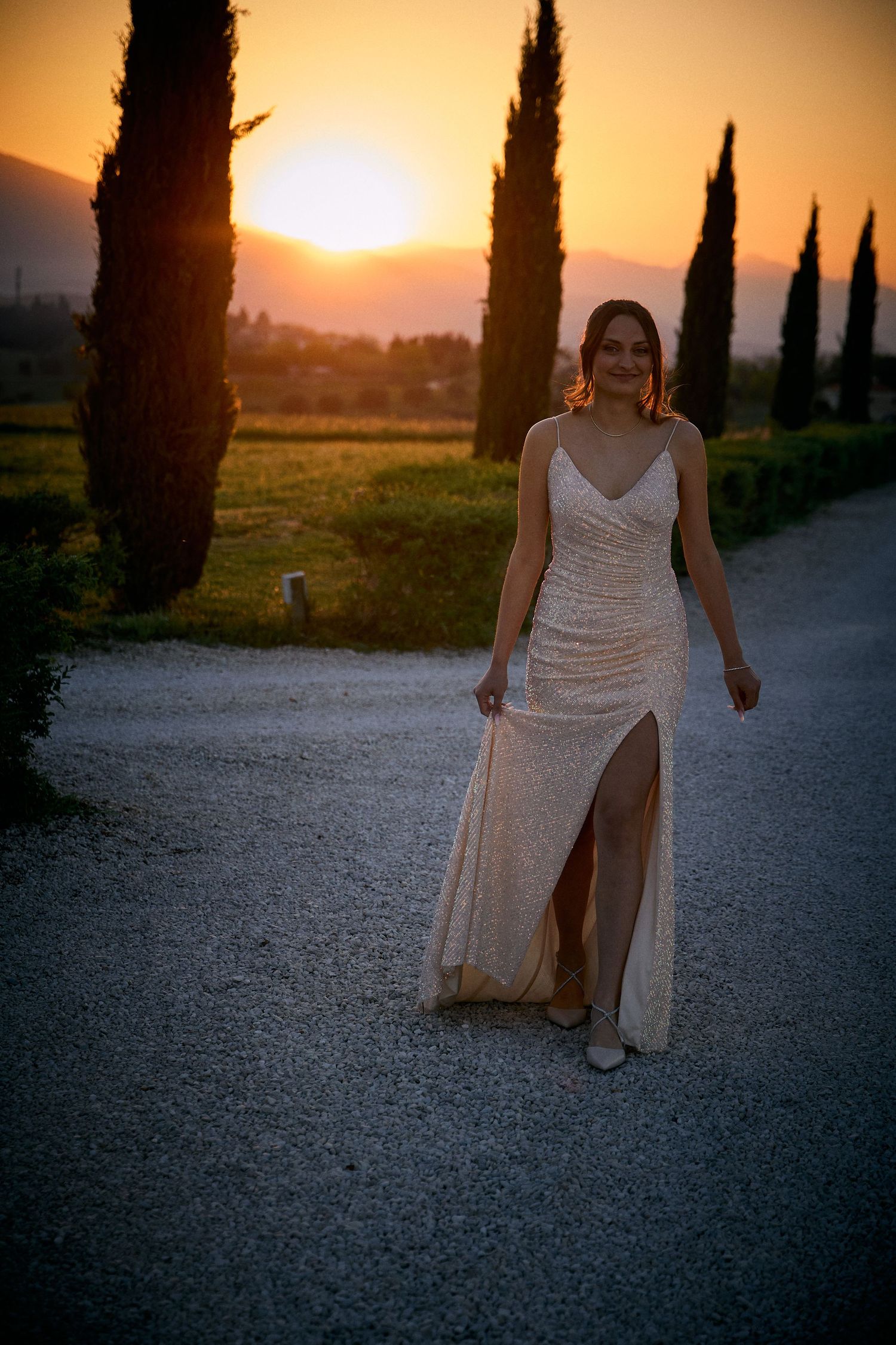 Elegant evening photo shoot with white dress against cypress trees and sunset backdrop.