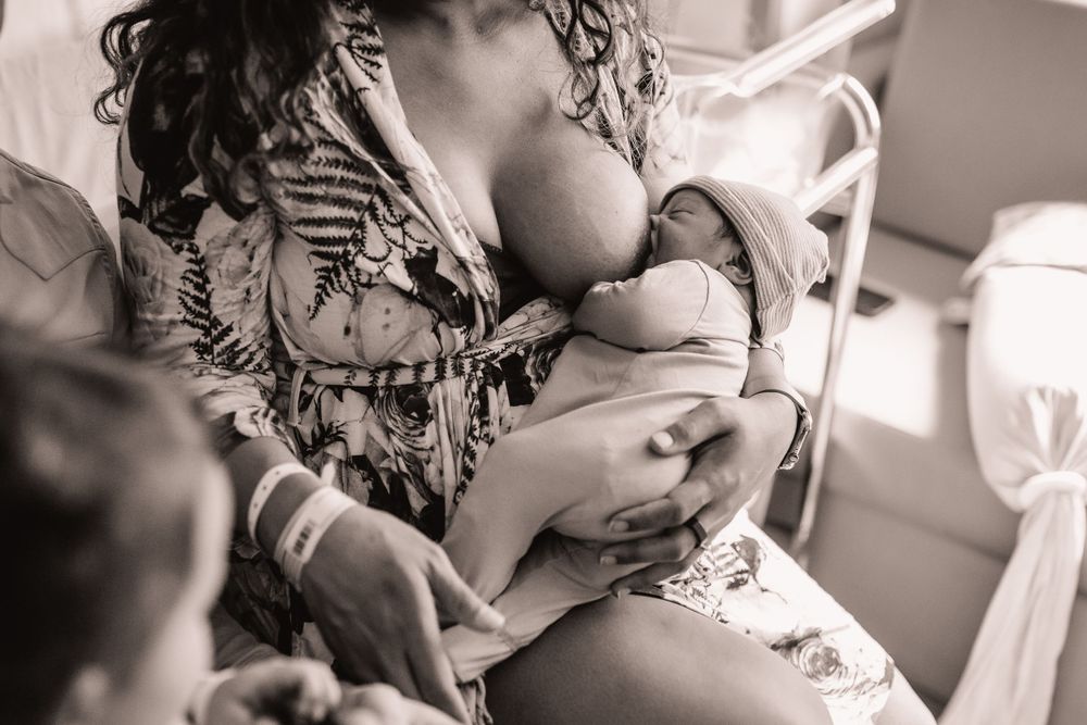 Mother breastfeeding her newborn baby in natural window light.
