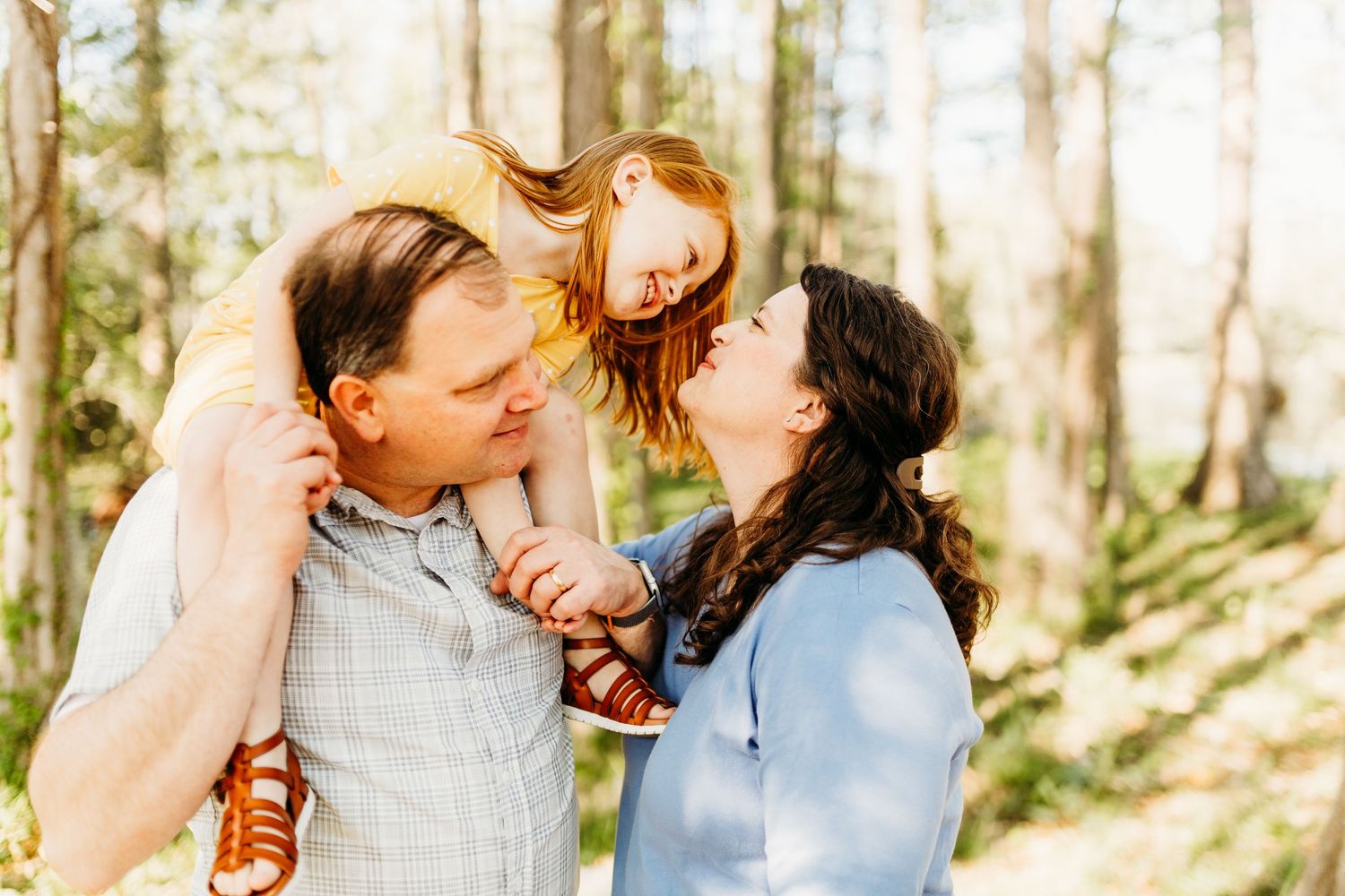 a little girl sits on dads shoulders and smiles at mom