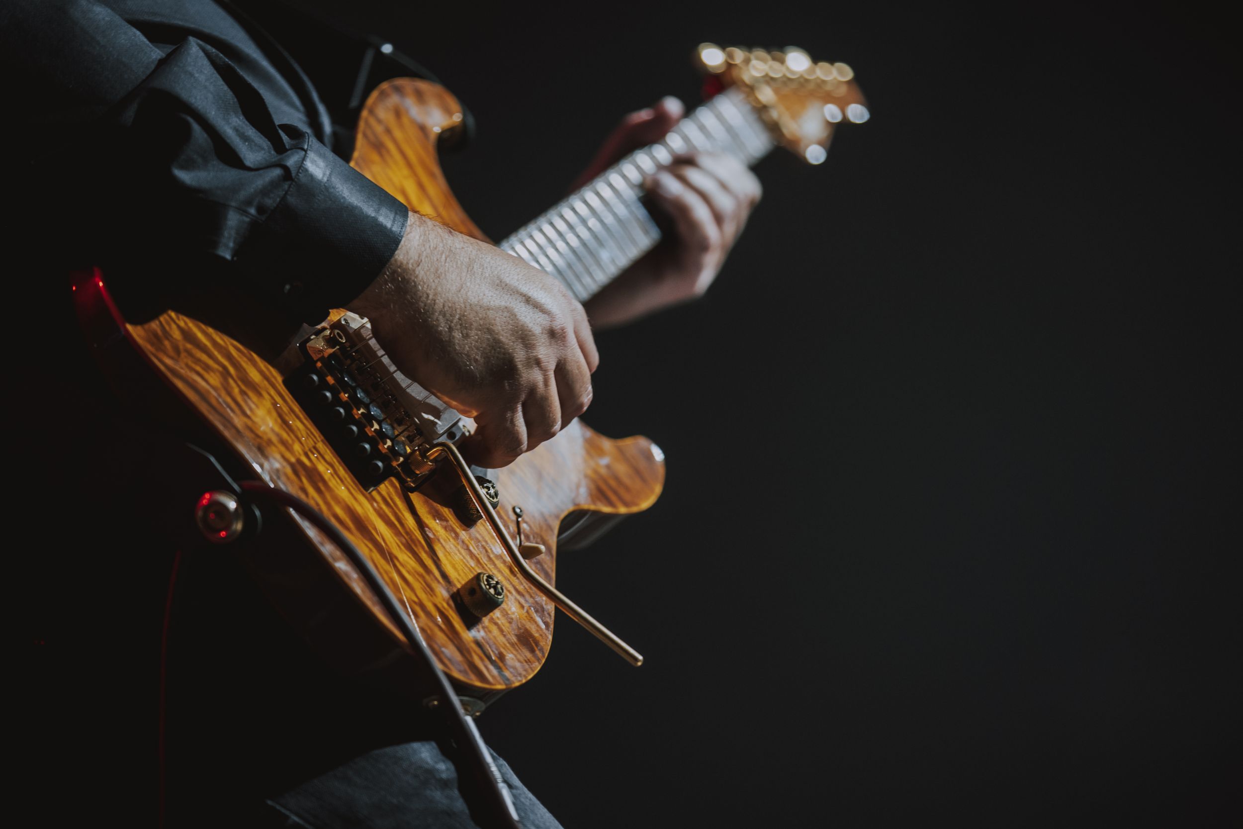 Close-up shot of hands playing a wooden electric guitar against a dark background.