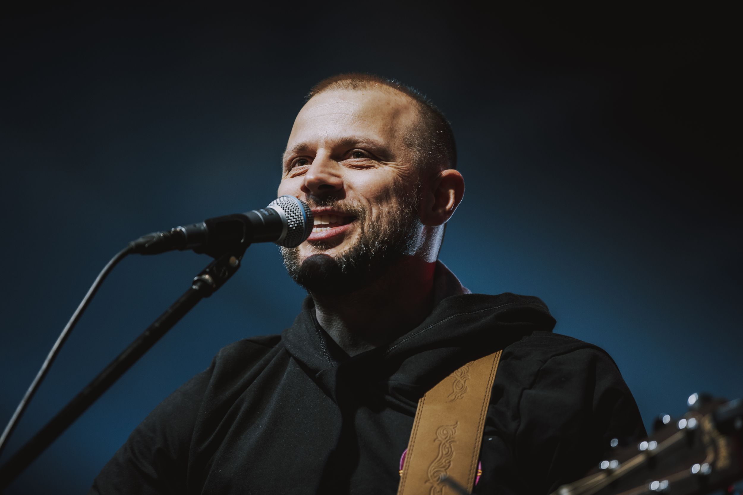A musician performing with an acoustic guitar under dramatic stage lighting.