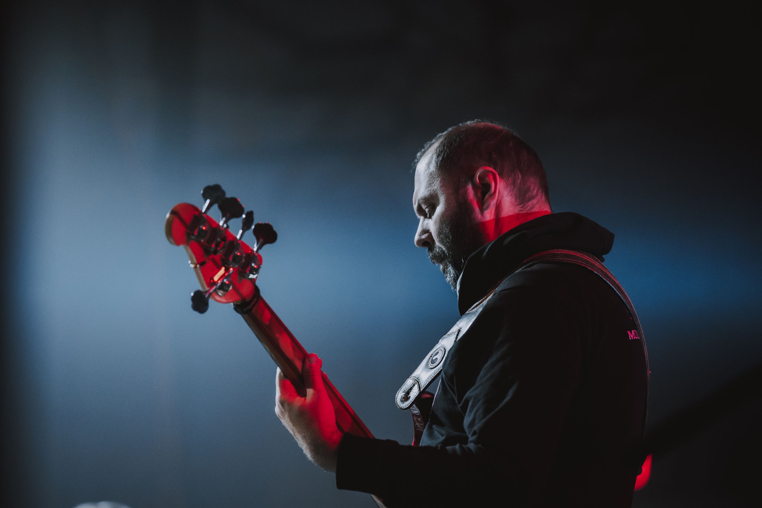 A bass guitarist performing on stage illuminated by blue and red lighting effects.