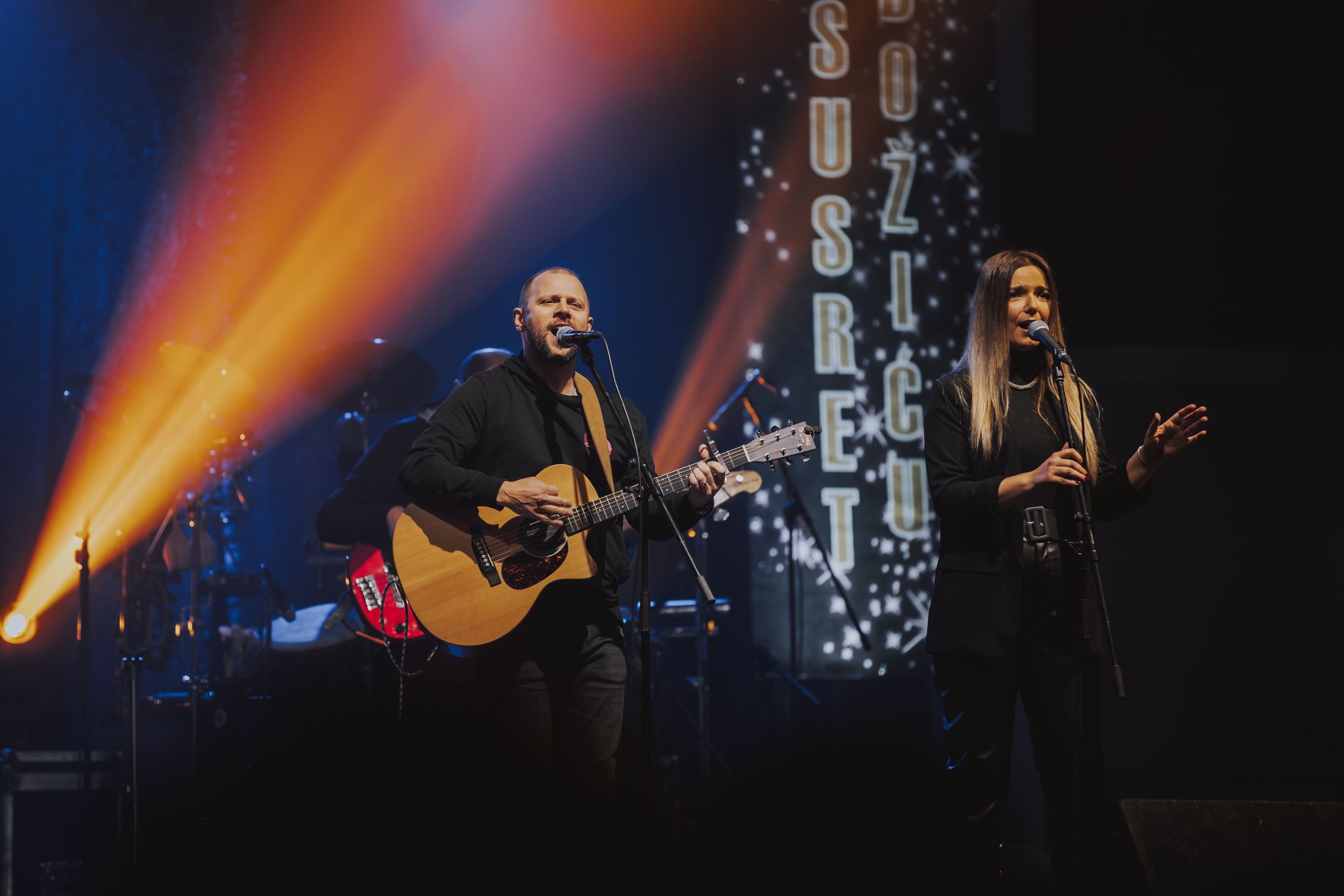 Musicians performing with acoustic guitar on stage with dramatic orange lighting effects.
