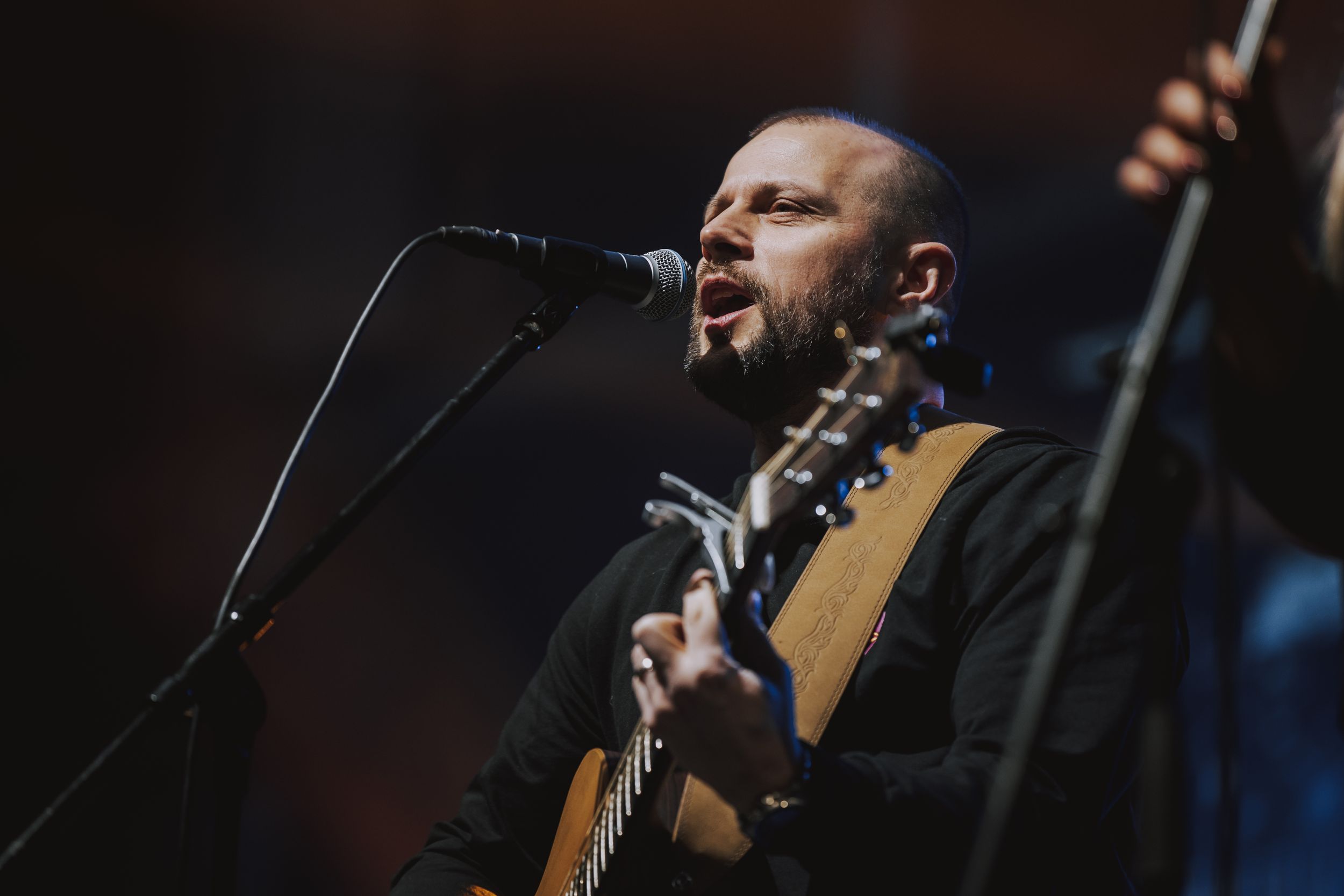 Musician performing with acoustic guitar under dramatic stage lighting.